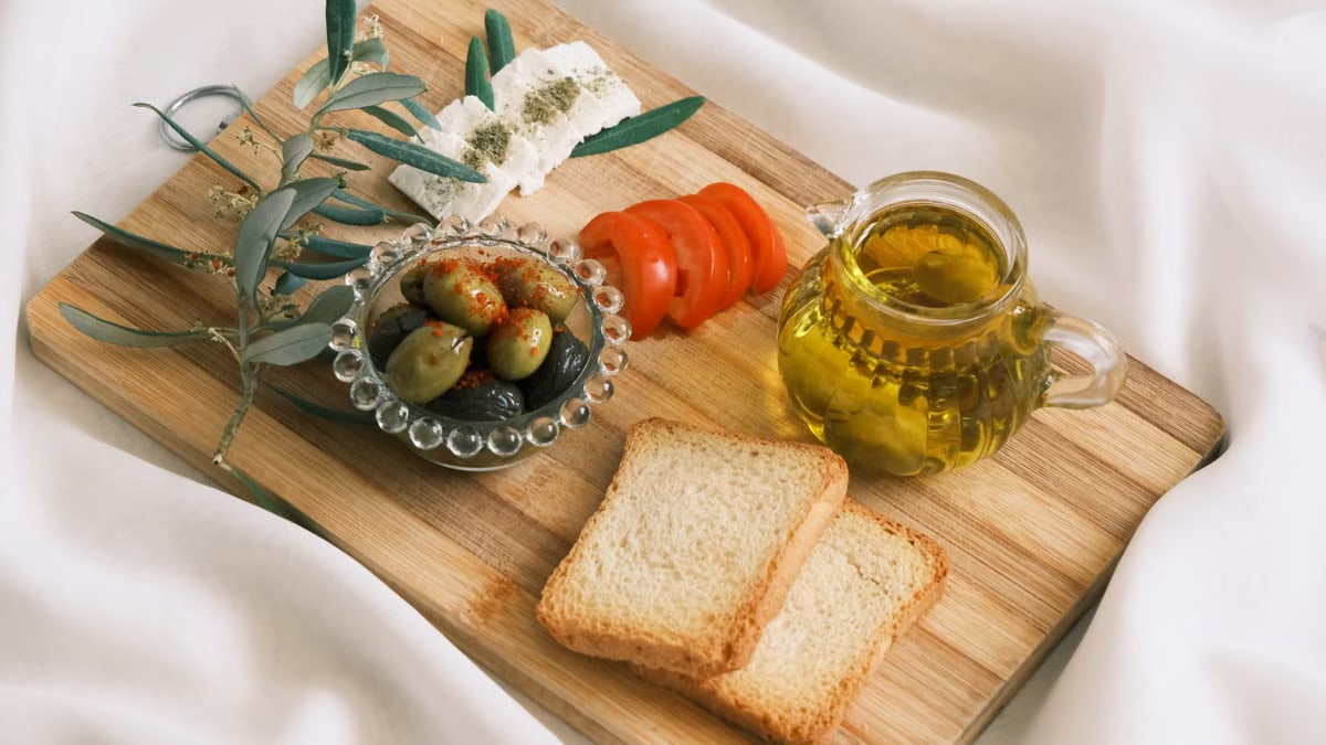 A rustic Mediterranean appetizer featuring olives, feta cheese, and olive oil on a wooden board.