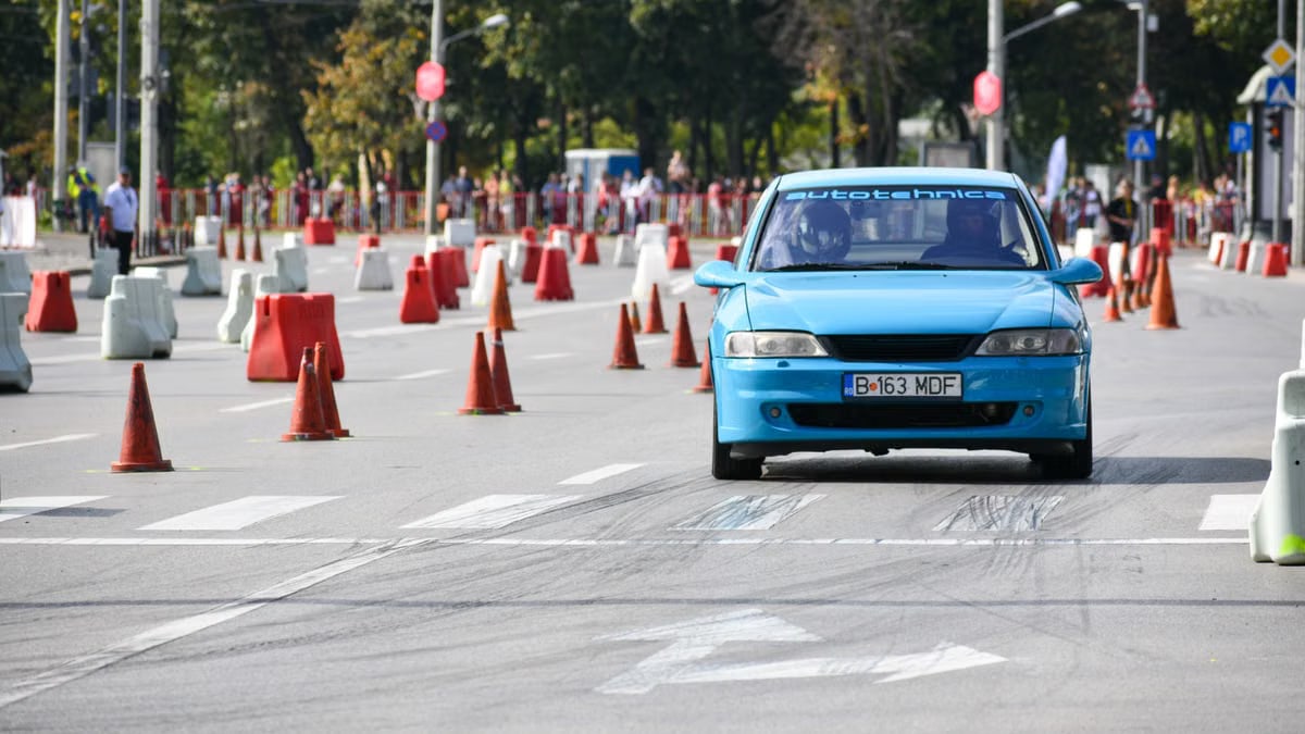 Blue car driving through an urban race course with traffic cones and onlookers.